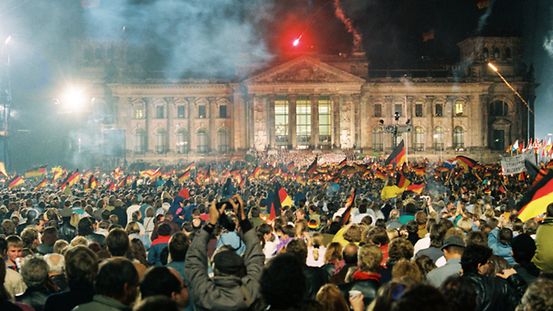 Blick auf den nächtlichen Reichstag. Dahinter ein Feuerwerk. Davor eine Menschenmasse mit vielen Deutschlandfahnen